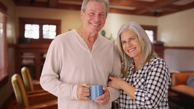 Lovely senior couple smiling, standing inside house kitchen