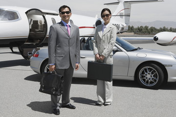 Full length of two happy business executives standing together at airfield with car and airplane in the background