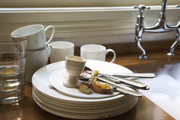Closeup of a stack of dirty dishes and silverware by sink in the kitchen
