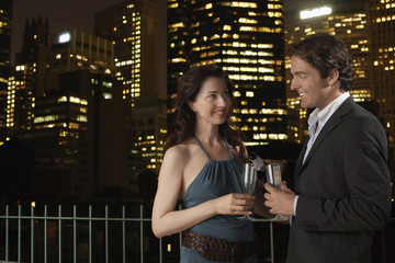 Elegant happy young couple with champagne flutes against cityscape at night