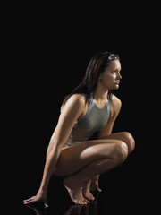 Full length side view of a female swimmer crouching against black background