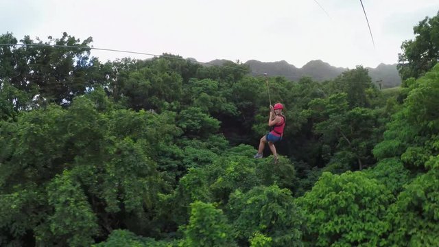 Young girl having fun while riding zipline cable above beautiful green jungle