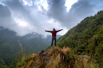 Fotobehang Reach out for the sky - A man opens out his arms facing a vibrant misty sky standing on top of a hill near Chungthang at North Sikkim, India. © Roop Dey