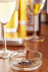 Cigarette in ashtray on table with glasses of wine