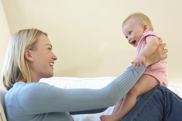 Side view of a happy young mother playing with baby boy on sofa at home