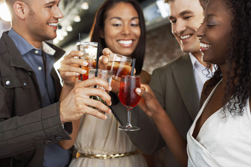 Two happy multiethnic couples toasting drinks at the bar