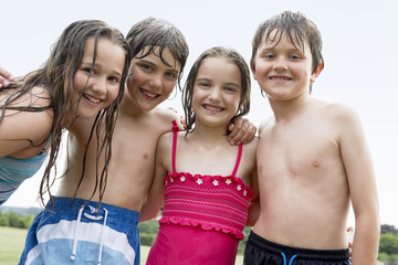 Portrait of four happy wet children in swimsuits standing against the sky