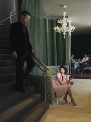 Full length of beautiful young woman waiting in hotel lobby with man descending staircase