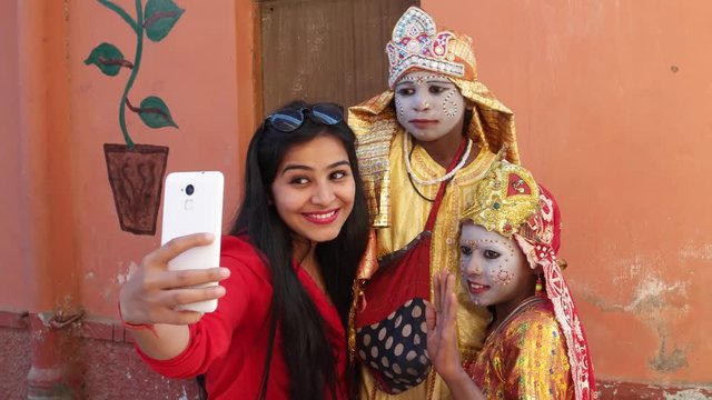 Indian traveller taking selfies with girls dressed as Hindu goddess with make-up and traditional clothing at the Pushkar Mela festival in Rajasthan, India 