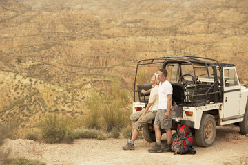 Middle aged couple in back of four-wheel-drive car on cliff edge in desert - Powered by Adobe