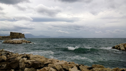 View of the restless Gulf of Naples with a great-looking wave and a castle (Castel Dell'ovo) in windy cloudy weather © kroshanosha