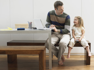 Father using laptop by daughter with cellphone at home