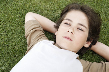 Closeup portrait of cute elementary boy with hands behind head lying on grass