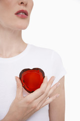 Closeup midsection of a woman in white tshirt holding red glass heart against white background