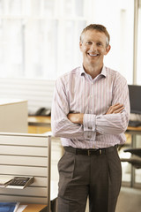 Portrait of middle aged male executive with hands folded smiling in office