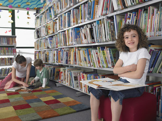 Portrait of a small girl reading book with people in the background