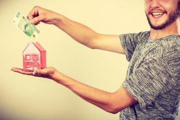 Man putting money into house piggybank