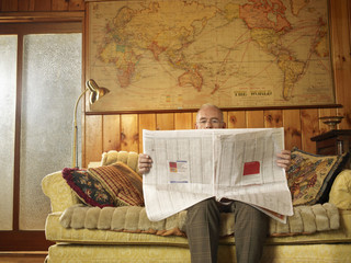 Senior man sitting on sofa reading newspaper in living room