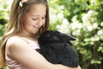 Happy young girl holding bunny rabbit in the backyard