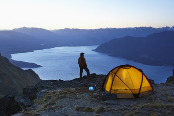 Man looking at lake by illuminated tent at dusk