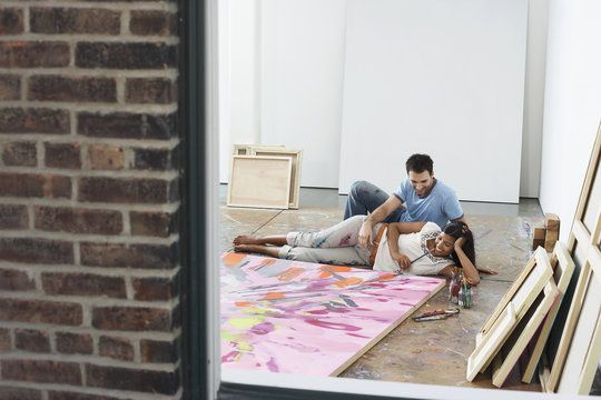 view through window of a couple reclining by painting on floor in studio