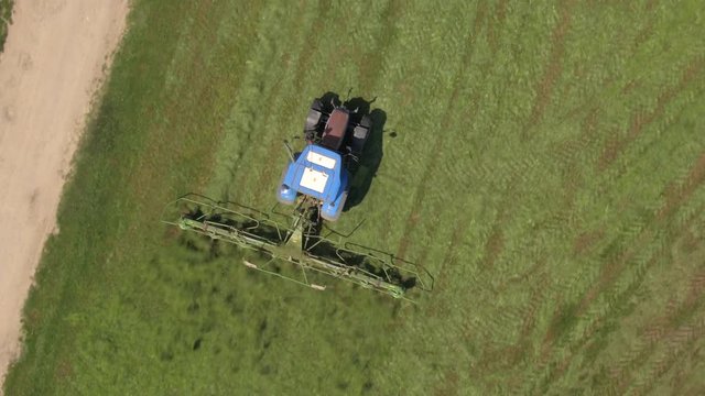 AERIAL: Flying above tractor turning mowed hay with tedder on farm field.  