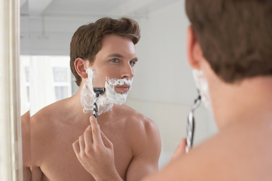 Reflection of a young man shaving in bathroom mirror