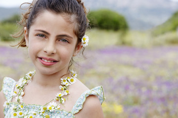 Portrait of happy cute little girl wearing necklace of flowers in field