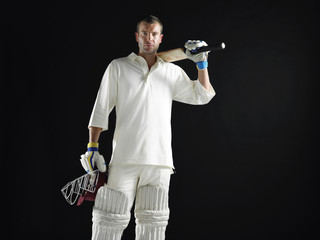 Portrait of a cricket player holding bat and helmet against black background