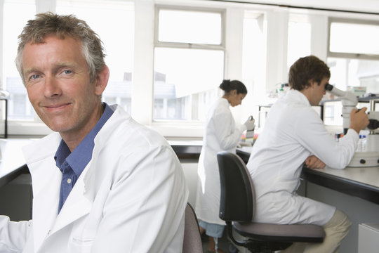 Portrait of happy male scientist with colleagues working in background