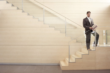 Confident businessman with newspaper looking away while standing on steps in office