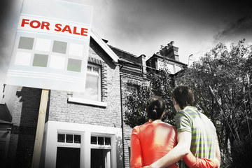 Rear view of young couple looking at new home with for sale sign