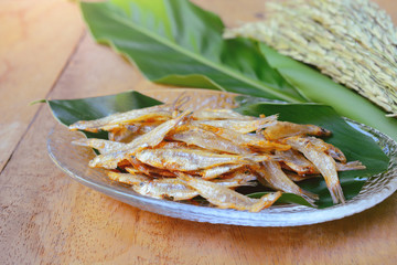 traditional thai fried small fish with green leaf on wooden background.