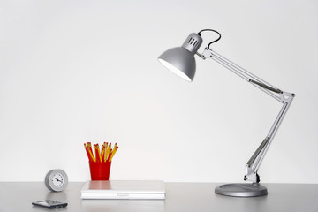 Angle poise lamp, laptop, clock, pencil holder and cellphone on desk