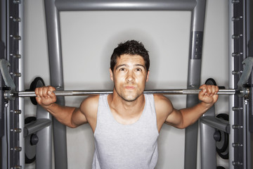 Portrait of young man struggling to lift weights at gym