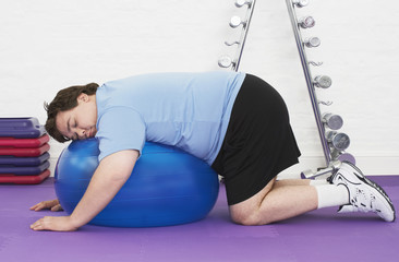 Side view of an overweight man sleeping on exercise ball in health club