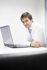  Portrait of a smiling young businessman sitting at desk with laptop