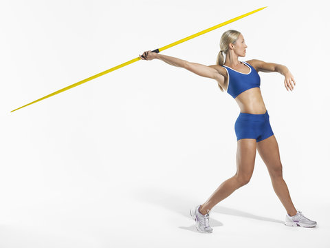 Full length side view of a female athlete preparing to throw javelin against white background