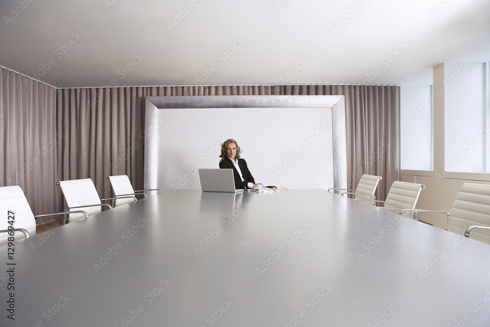 Wall mural female business executive sitting alone in boardroom with laptop