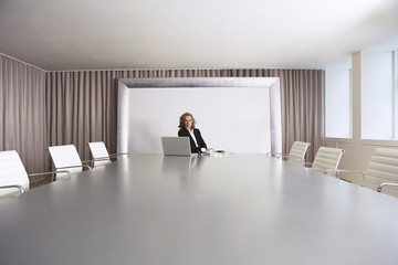 Female business executive sitting alone in boardroom with Laptop