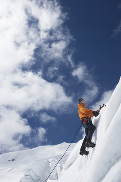 Low angle view of a male mountain climber going up snowy slope with axes against clouds