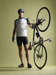 Full length of a bicyclist standing alongside bicycle against colored background