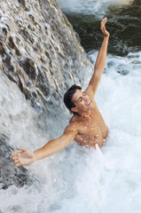 High angle view of happy young man with arms outstretched enjoying in waterfall