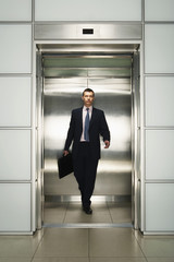 Front view of middle aged businessman with briefcase coming out from elevator © MDBPIXS
