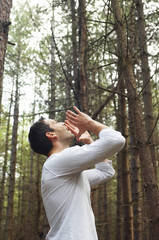 Low angle side view of a young man standing alone in woods and yelling
