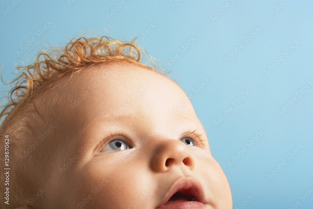 Wall mural Closeup of cute baby boy looking up isolated on blue background