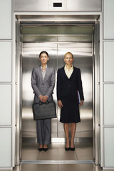 Two confident businesswomen in formal wear standing together in elevator