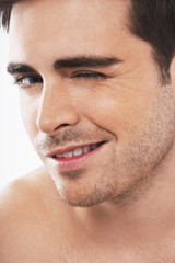 Fototapeta premium Closeup of flirtatious young man winking on white background