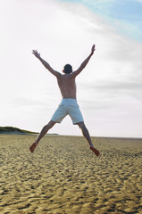 Rear view of a young shirtless man doing star jump on beach