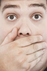 Extreme closeup portrait of an overweight man with hand on mouth and raised eyebrows